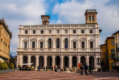 People in front of building against cloudy sky