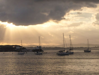 Sailboats sailing in sea against sky during sunset