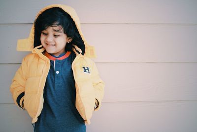 Cute boy with hands in pockets standing against wall