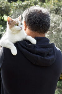 Rear view of mature man walking in a park with a cat on his shoulder.