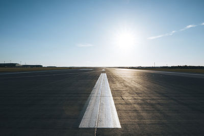 Surface level of long airport runway with directional marking against clear sky on sunny day.