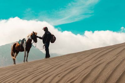 Men riding horse on sand against sky