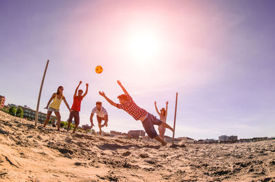 People playing with ball on beach against sky