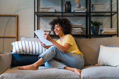 Young woman using tablet pc while sitting on sofa at home