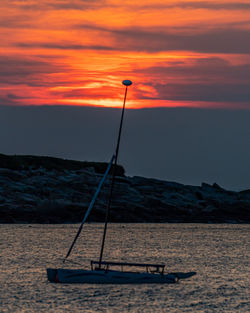 Isolated sailboat as the sun sets beyond clouds in the distance.