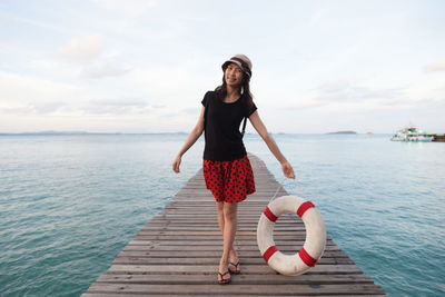 Full length of woman holding inflatable ring while standing on pier over sea against sky