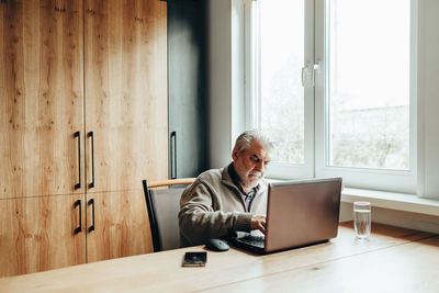 An elderly man works at a laptop, learning from home, home bookkeeping