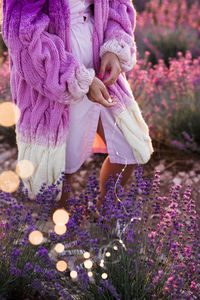 Woman wearing stylish knitted cardigan posing in lavender field picking flowers outdoors. 