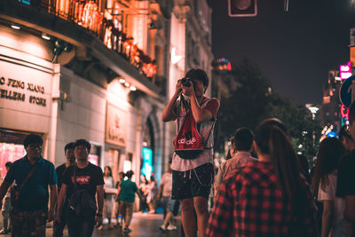 People photographing on illuminated street in city at night