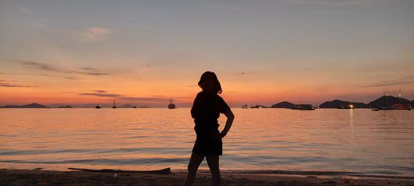 Rear view of silhouette woman standing on beach during sunset