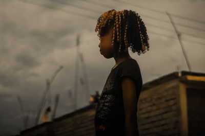 Girl with curly hair standing against sky