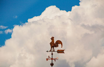 Weather vane against cloudy sky