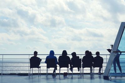 People sitting on chairs at beach against cloudy sky