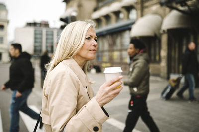 Contemplative businesswoman holding disposable cup while crossing street in city