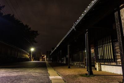 Illuminated street amidst buildings against sky at night