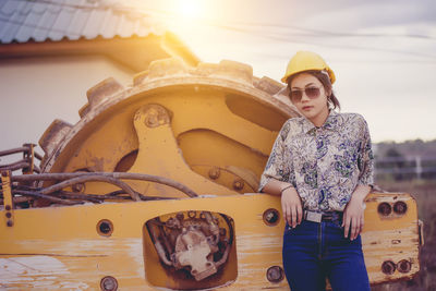 Portrait of young woman wearing hardhat while standing by construction vehicle