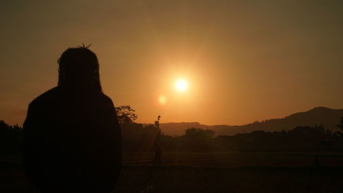 Silhouette man standing on field against sky during sunset