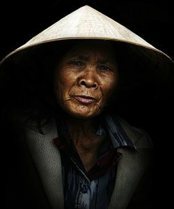 Portrait of senior woman wearing asian style conical hat against black background