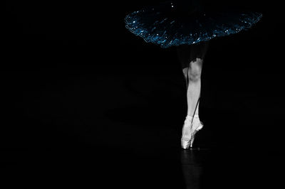 Low section of ballet dancer against black background