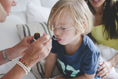 Grandmother feeding medicine to boy with woman sitting in background