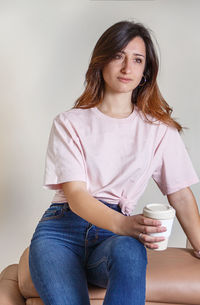 Portrait of beautiful young woman sitting against wall