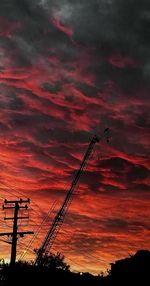 Low angle view of silhouette electricity pylon against dramatic sky during sunset