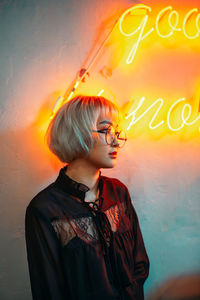 Woman wearing sunglasses looking away while standing by wall