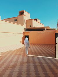 Rear view of woman walking on footpath against buildings