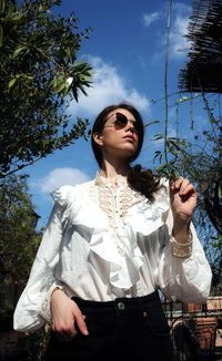 Portrait of young woman wearing sunglasses standing against sky