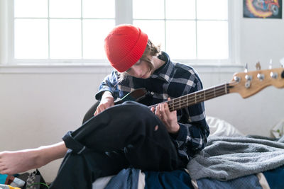 Musician sitting on edge of bed playing guitar in bright sunny room