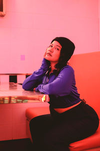 Portrait of young woman sitting at table against wall