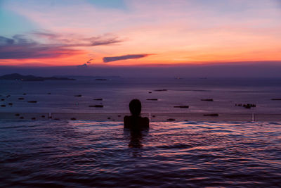 Rear view of silhouette woman in infinity pool against sea during sunset