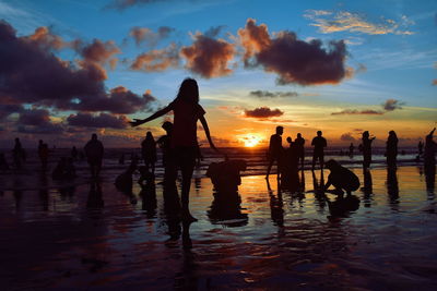 Silhouette people at beach against cloudy sky during sunset