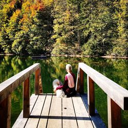 Woman sitting on wooden footbridge over lake