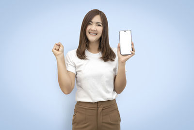 Portrait of smiling young woman using smart phone against clear sky