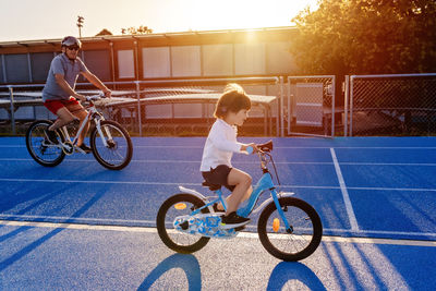 Happy smiling toddler boy riding bicycles together with grandfather having fun outdoors at sunset