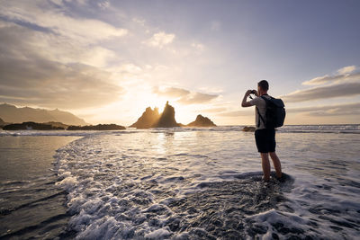 Man during photographing landscape with cliff. young photographer on beach at beautiful sunset. 