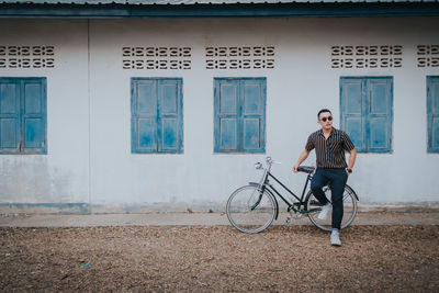 Full length of man sitting outside house on bicycle