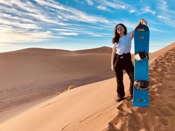 Woman standing on sand dune in desert against sky