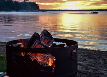 Close-up of illuminated fire pit at beach during sunset