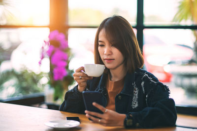 Young woman drinking coffee while sitting on table at cafe