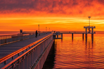 Pier over sea against dramatic sky during sunset