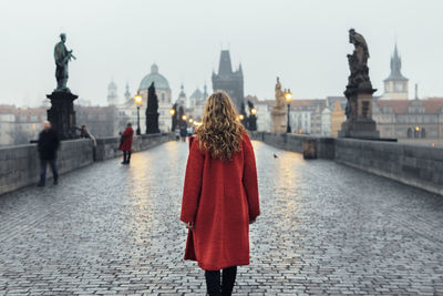 Rear view of woman walking on bridge by street lights at sunrise