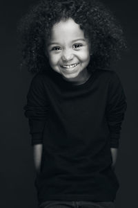 Portrait of young woman standing against black background