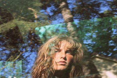 Portrait of young woman against tree trunk reflecting on window