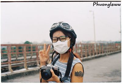 Portrait of young woman photographing against sky