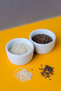 Wooden spoons with sesame and flax seeds lies in a white mortar on a yellow background. healthy