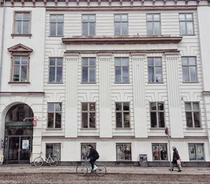 People riding bicycle on street against building