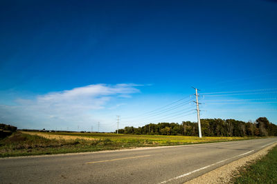 Road by electricity pylon against blue sky