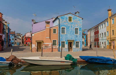 Boats moored on canal by buildings in city against sky